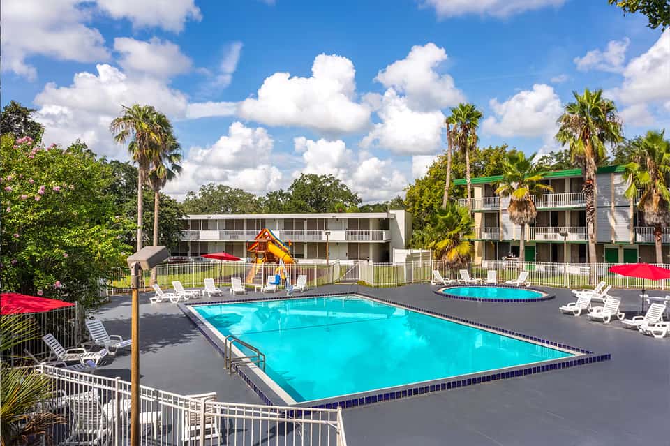Bright blue resort pool with white loungers, palm trees, and multi-story hotel buildings