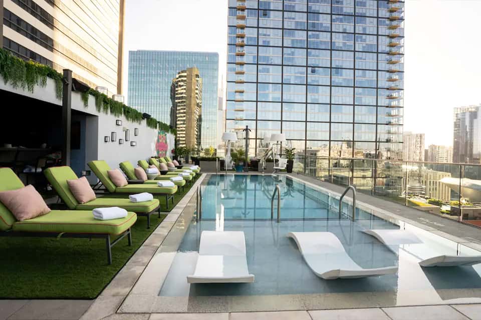 Rooftop pool with city views, lime green lounge chairs, and white cushioned loungers