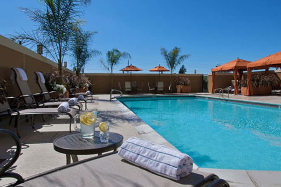 Resort pool area with loungers, orange umbrellas, palm trees, and tan building backdrop