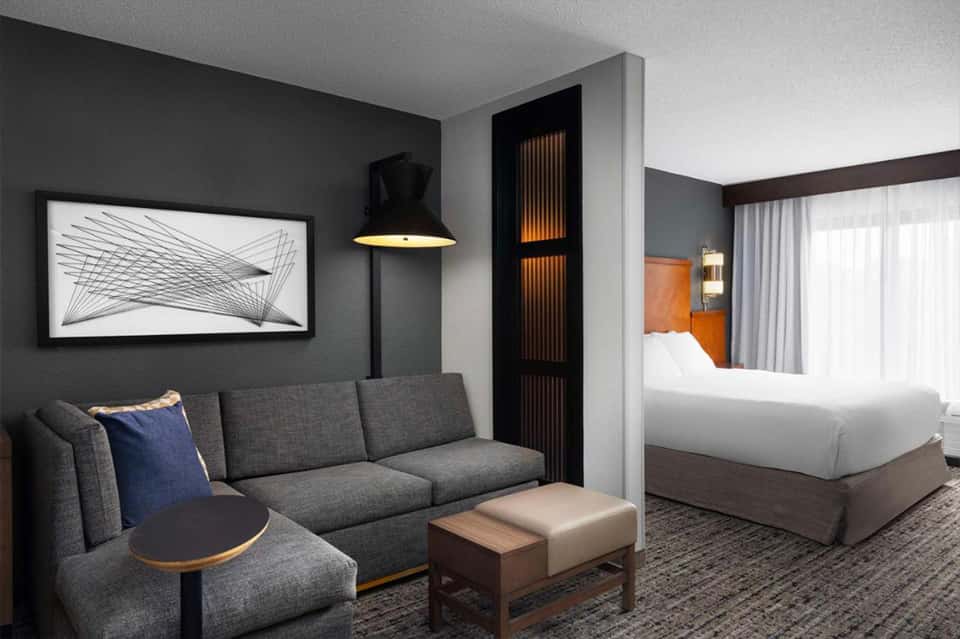 Modern hotel suite with gray sofa, king bed, abstract wall art, pendant lamp, and minimalist design