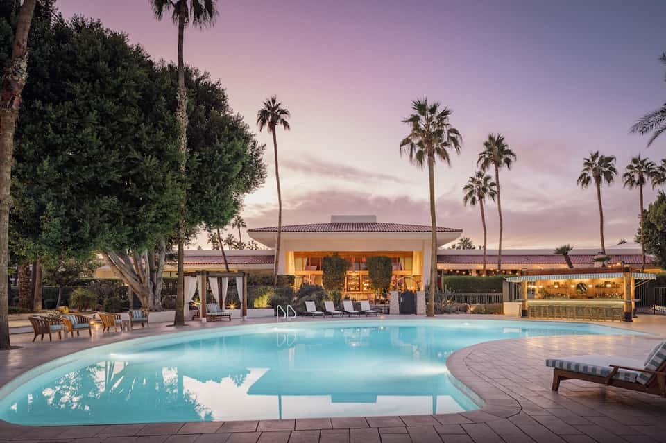 Luxury pool at dusk with lit clubhouse, palm trees, and lounge seating