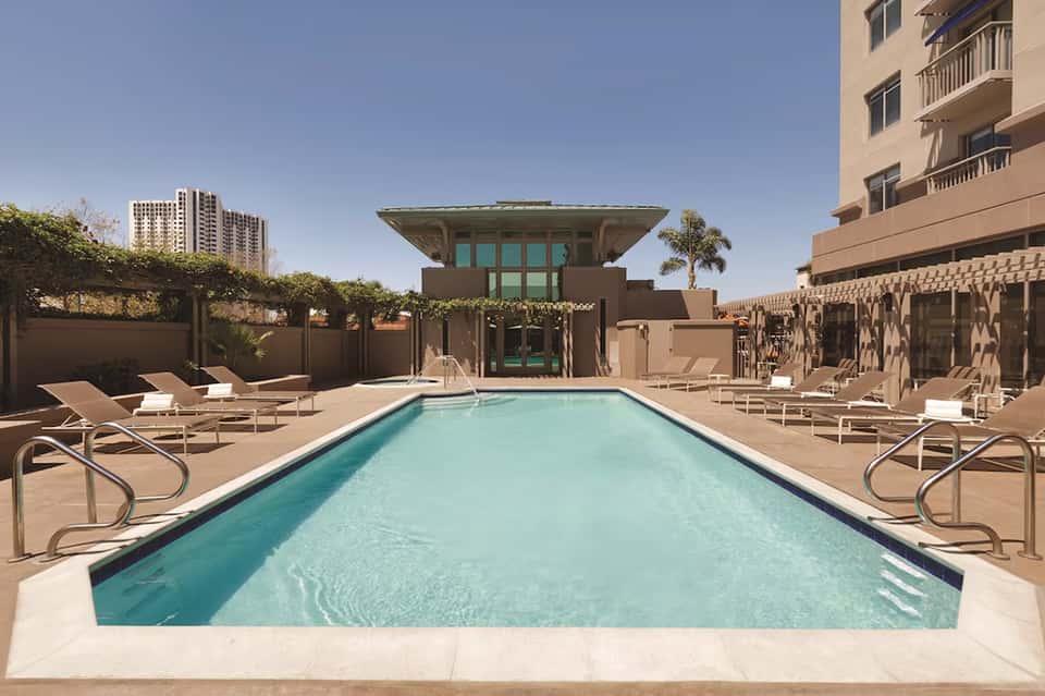Modern rooftop pool with geometric architecture, turquoise water, lounge chairs, and city views