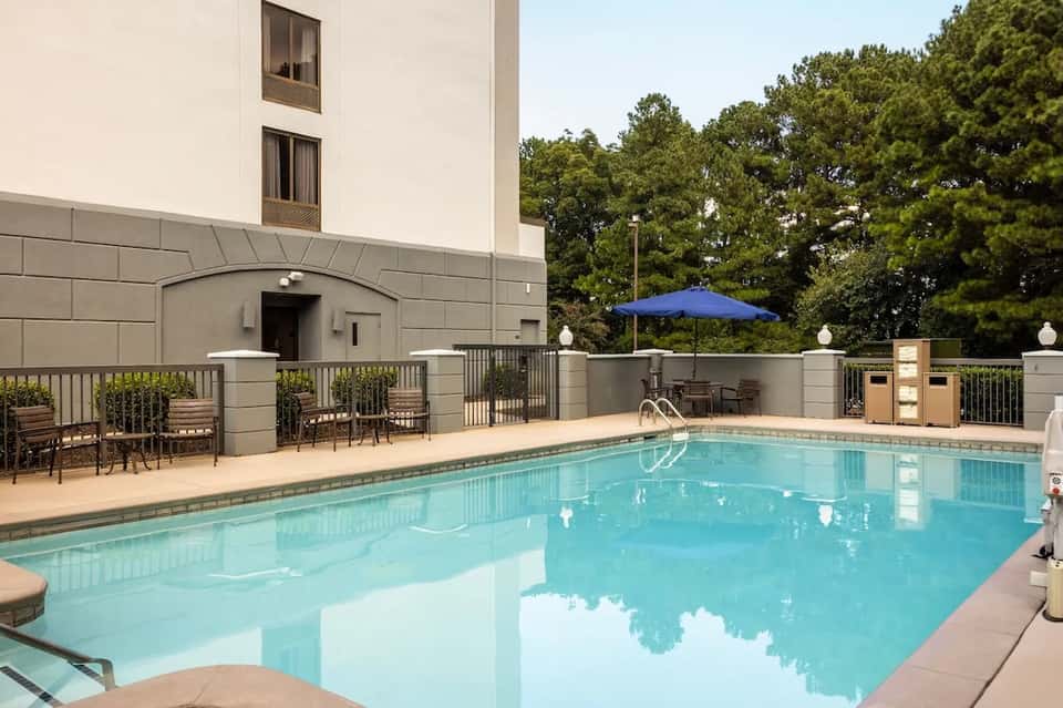 Indoor swimming pool with blue umbrella, lounge chairs, and building exterior view