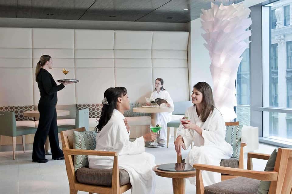 Modern spa lounge with women in robes, geometric wall art, wooden furniture, and floor-to-ceiling windows