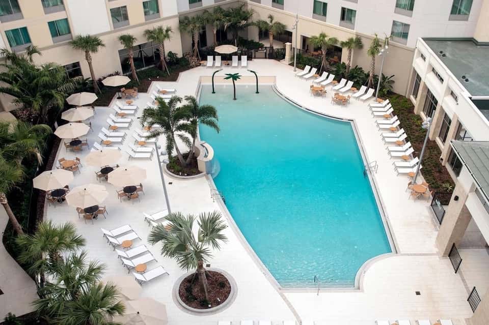 Aerial view of resort courtyard with turquoise pool, palm trees, and lounge chairs