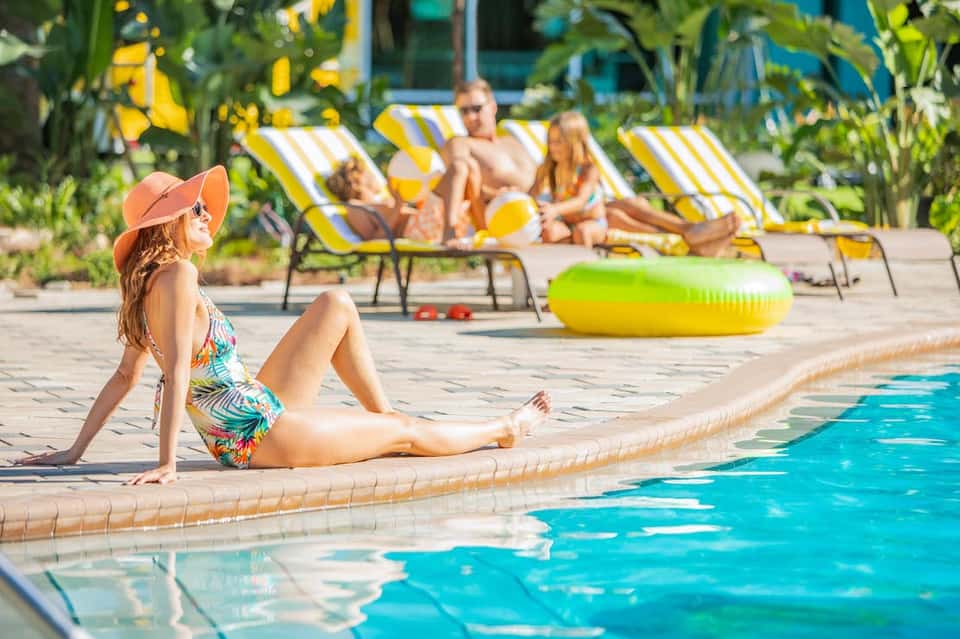 Resort pool scene with guests relaxing on striped loungers and swimming in turquoise water