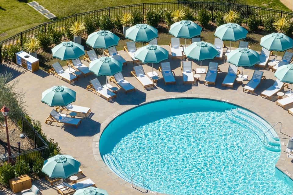 Resort pool surrounded by teal umbrellas and lounge chairs with landscaped lawn area