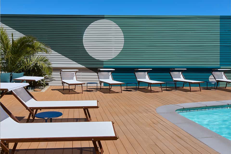 Modern poolside deck with turquoise pool, white lounge chairs, and teal accent wall