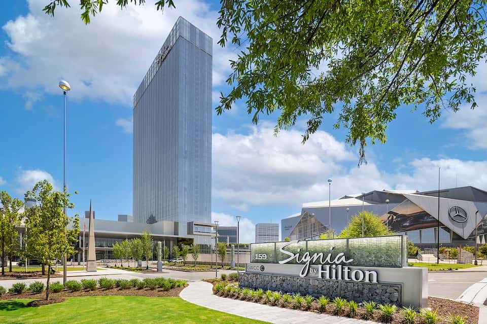 Modern Sigma by Hilton hotel exterior with tall glass tower, manicured landscaping, and street entrance