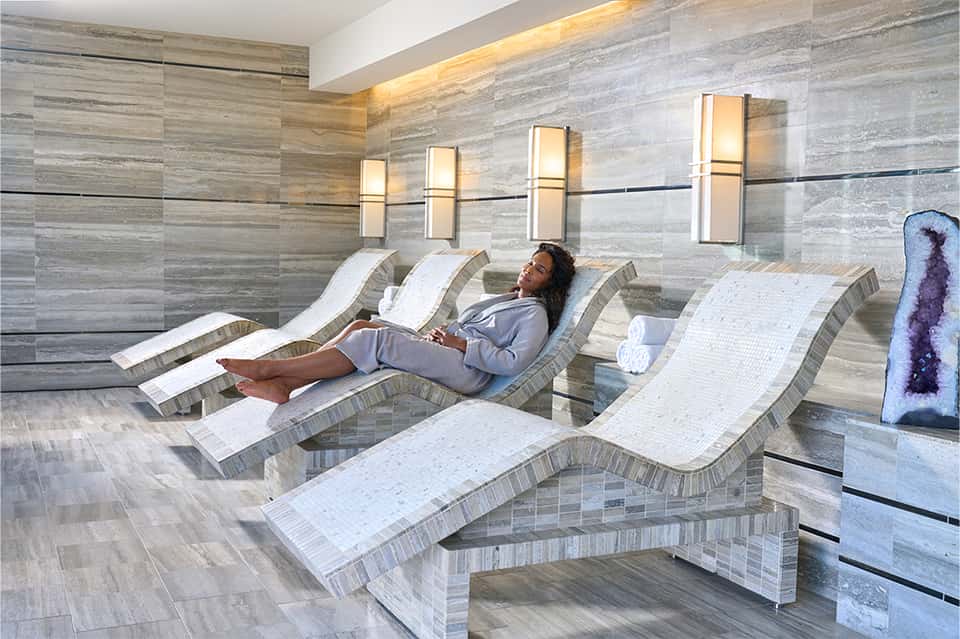 Modern spa relaxation room with curved lounge chairs, gray tile walls, and ambient lighting