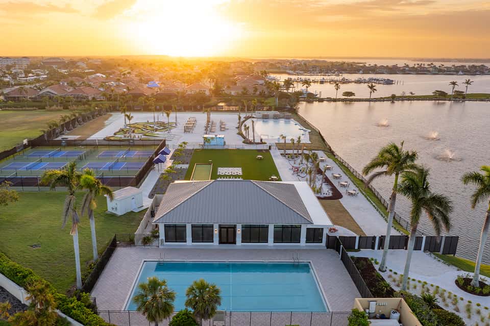 Aerial sunset view of resort with pools, sports courts, waterfront, and palm trees