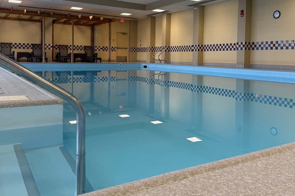 Empty indoor lap pool with blue water, checkered tile walls, and accessible ramp for swimmers