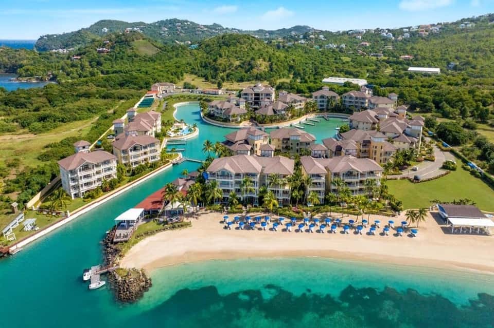 Aerial resort view with multiple pools, beachfront, colorful umbrellas, and lush green hillside