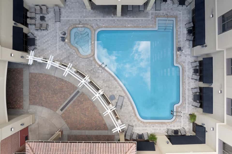 Overhead view of resort pool deck with hot tub, lounge chairs, and surrounding buildings