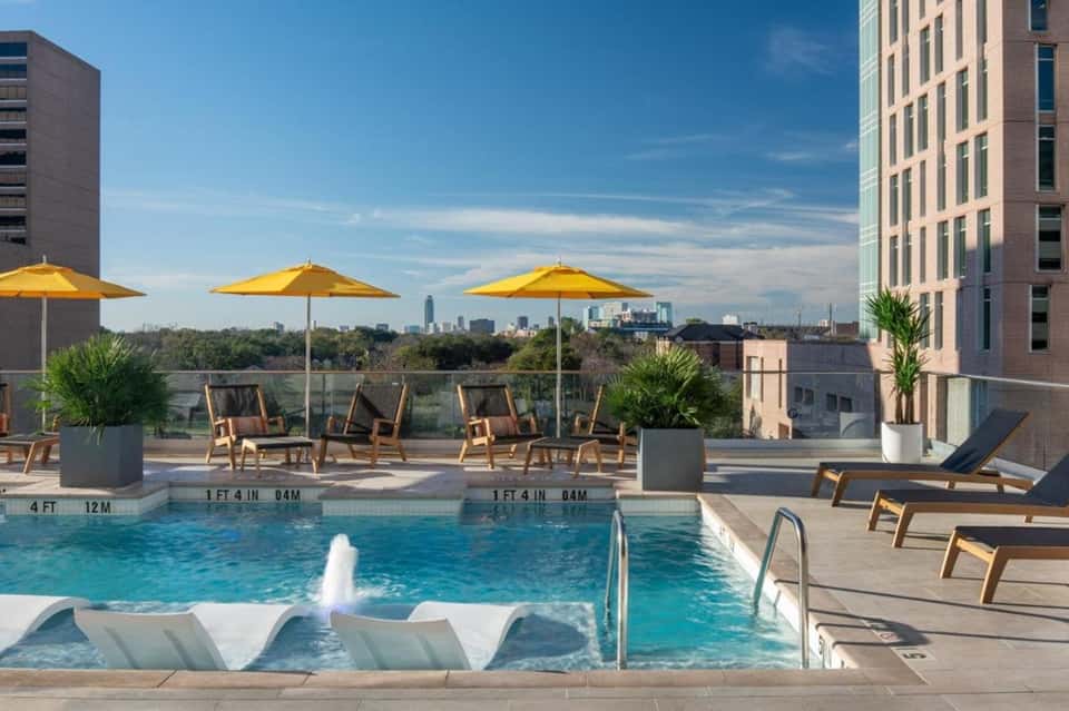 Rooftop pool deck with yellow umbrellas, lounge chairs, city skyline views, and modern urban architecture