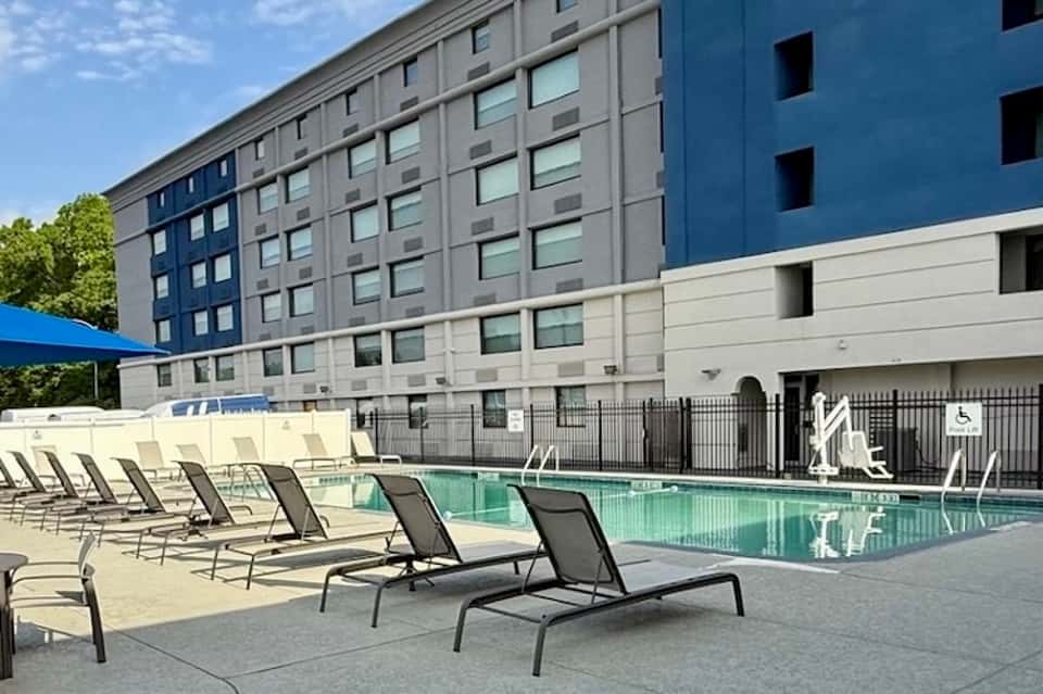 Hotel exterior with pool, striped lounge chairs, multi-story building with blue and gray facade