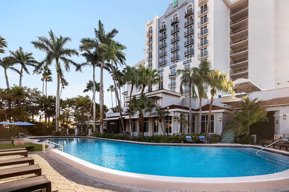 Resort exterior with palm trees, white hotel building, and curved swimming pool