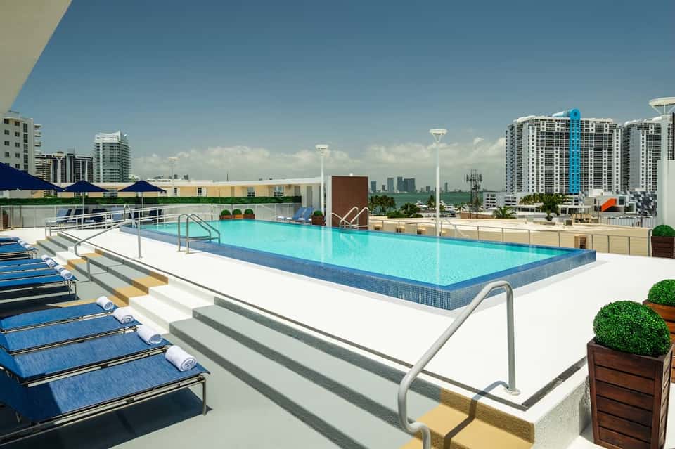 Rooftop swimming pool with blue loungers, umbrellas, and city skyline visible in background