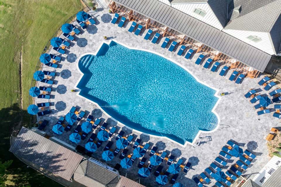 Aerial view of kidney-shaped pool with blue umbrellas, loungers, and landscaped grounds