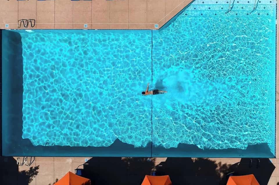 Overhead view of rectangular swimming pool with swimmer and lounge chairs on deck