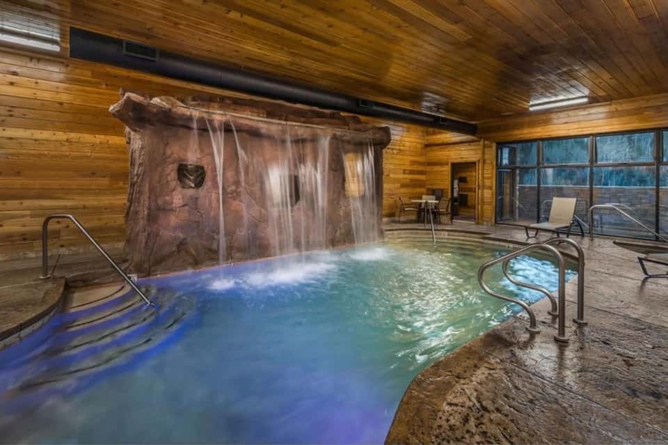 Indoor geothermal pool with natural hot spring waterfall, wooden ceiling, and lounge seating