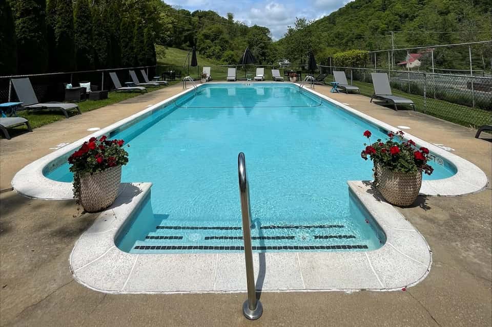 Resort lap pool with red flower planters, lounge chairs, umbrellas, and green hillside backdrop
