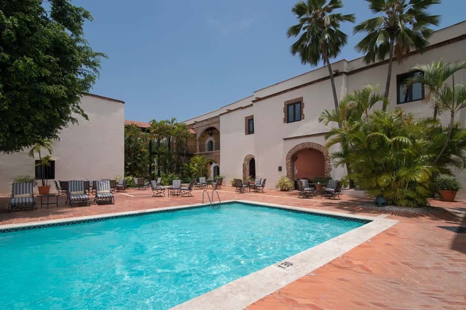 Pool courtyard with arched architecture, striped lounge chairs, and palm trees