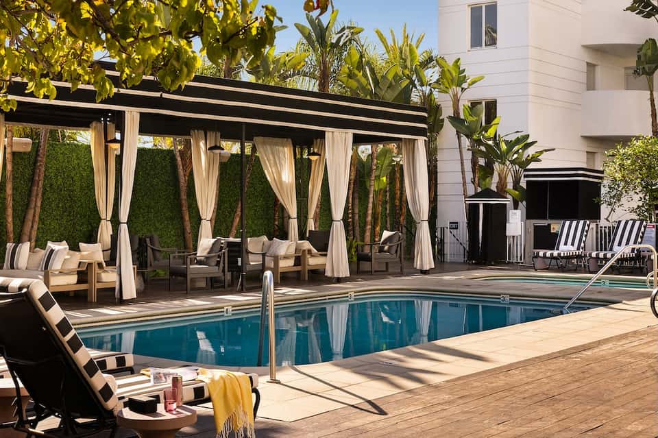 Luxury resort pool with black pergola cabanas, cream curtains, palm trees, and white building facade