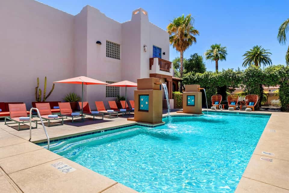Pink building with turquoise pool, lounge chairs, orange umbrellas, and desert landscaping