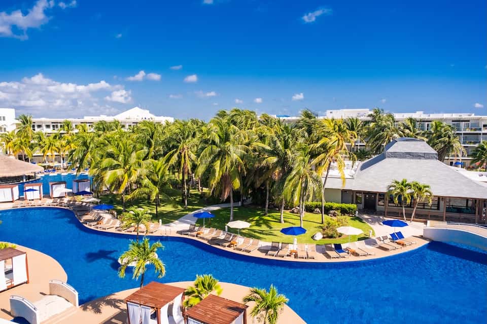 Aerial view of sprawling resort with curved blue pools, palm trees, loungers, and tropical grounds