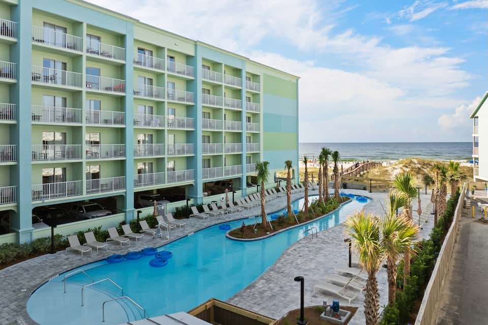 Beachfront resort with turquoise pool, palm trees, and ocean view from balcony