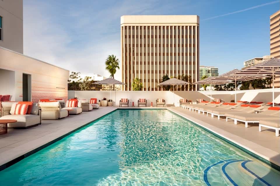 Urban rooftop pool with turquoise water, loungers, umbrellas, and high-rise backdrop