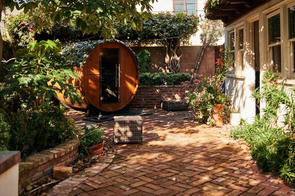 Round wooden sauna structure in lush garden courtyard with tropical plants
