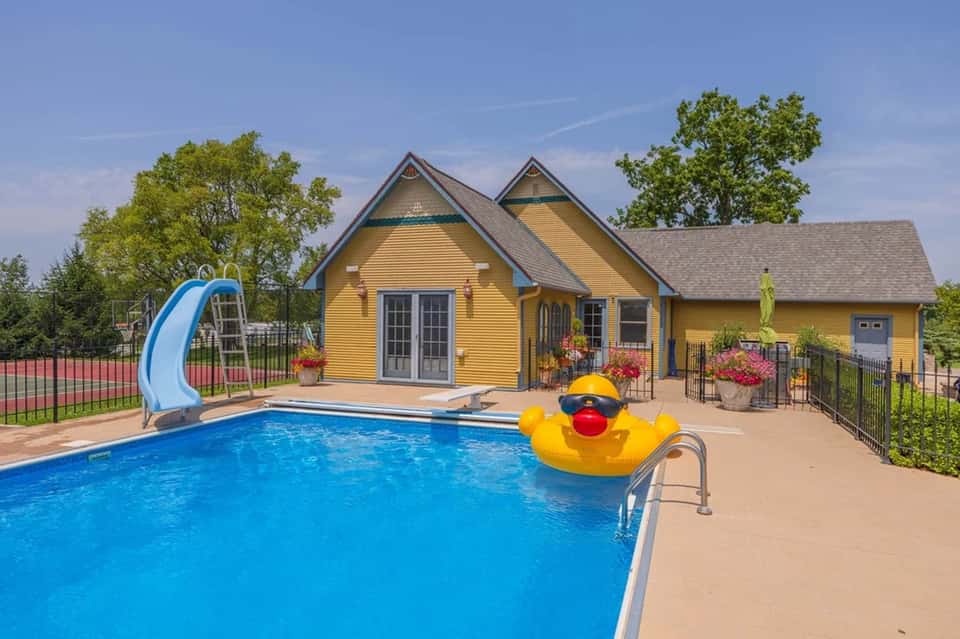 Yellow cottage-style poolhouse with blue water slide and yellow duck float in sparkling pool