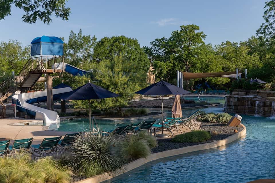 Water park with blue slide tower, multiple pools, umbrellas, and surrounding trees