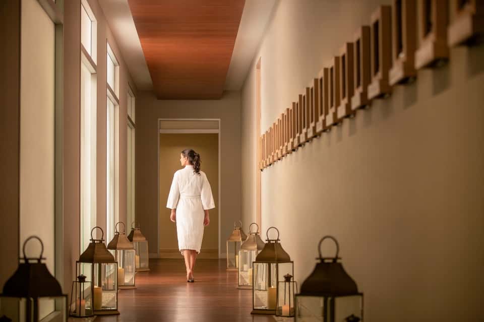 Spa corridor with woman in white robe walking between decorative lanterns and wood-slat wall accents