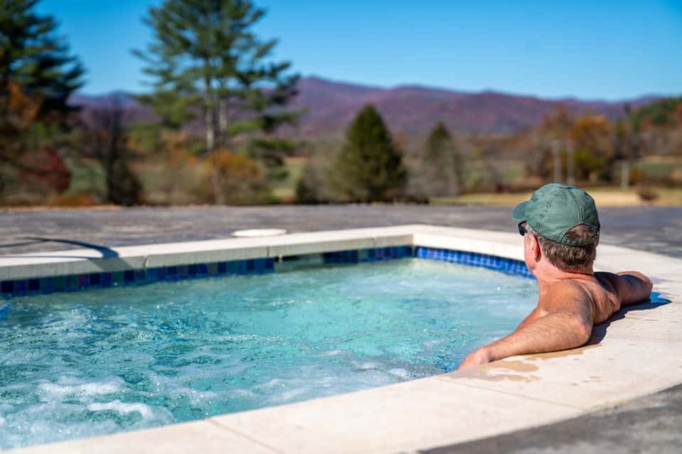Man relaxing in hot tub with mountain and forest backdrop