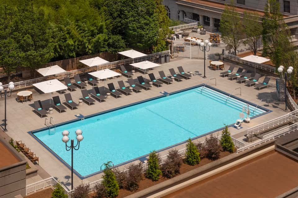 Aerial view of resort pool deck with lounge chairs, umbrellas, and surrounding high-rise