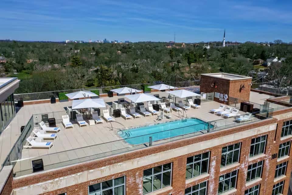 Rooftop pool deck with white umbrellas, lounge chairs, brick building, and city skyline view