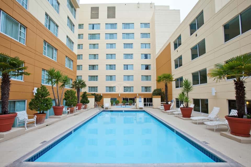 Indoor courtyard pool surrounded by multi-story hotel building with warm-toned exterior and tropical landscaping