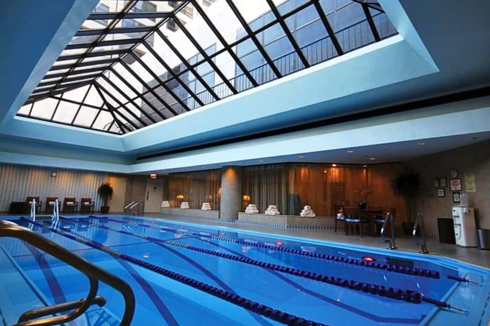 Indoor lap pool with lane dividers under glass skylight ceiling and warm lighting