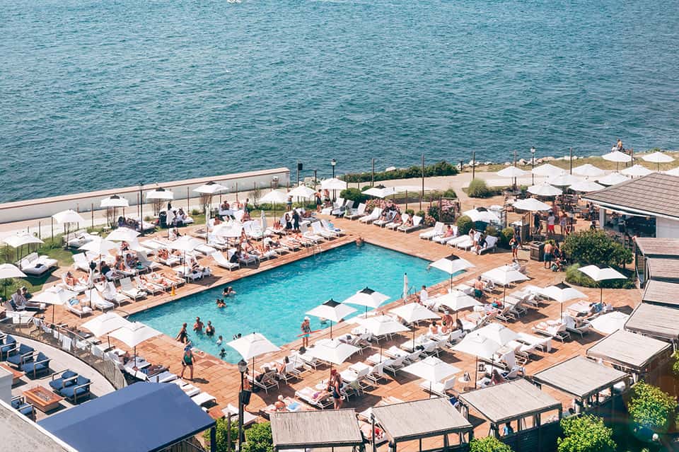 Aerial view of resort pool with white loungers, umbrellas, beach access, and coastal views