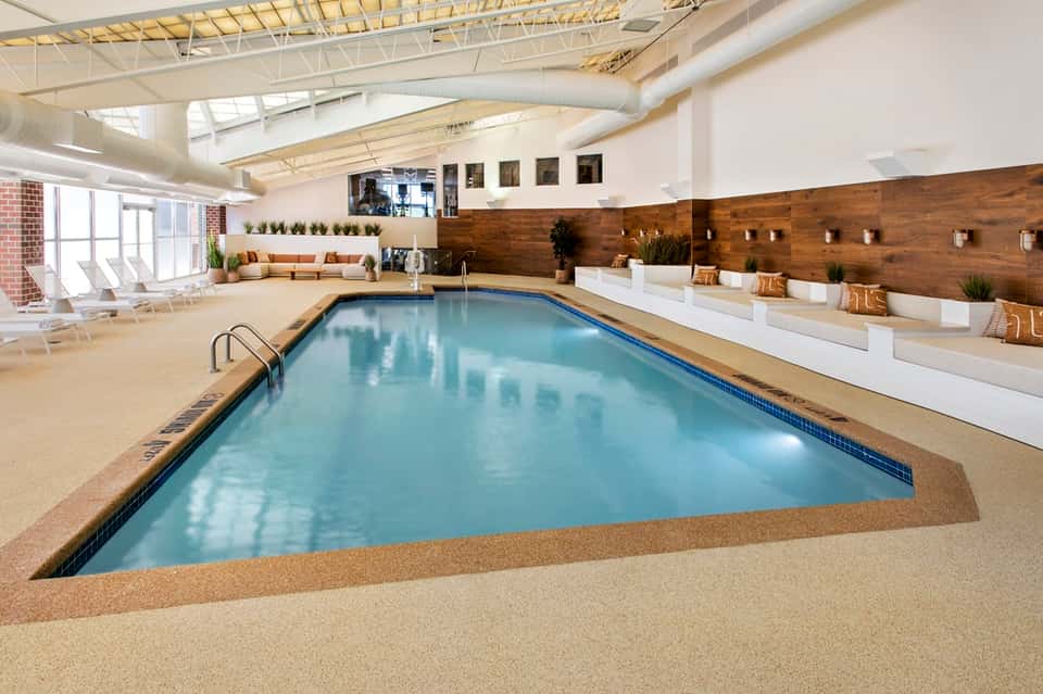 Modern indoor pool with high ceiling, skylights, wooden accents, and lounge seating areas