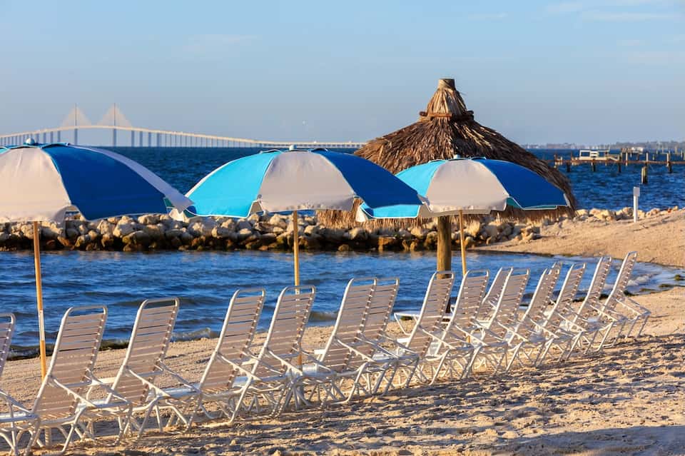 Beach lounge area with blue and white umbrellas, chairs, and bridge spanning water