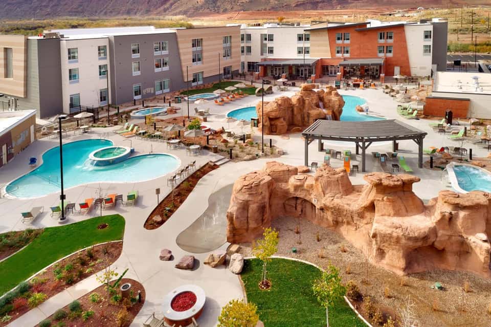 Aerial view of resort complex with multiple pools, red rock formations, residential buildings, and desert landscape