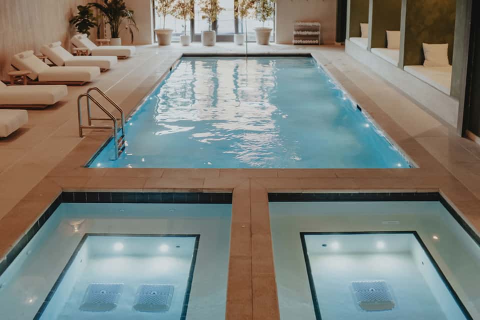 Indoor pool facility with lap lanes, cream loungers, and spa amenities in modern beige setting
