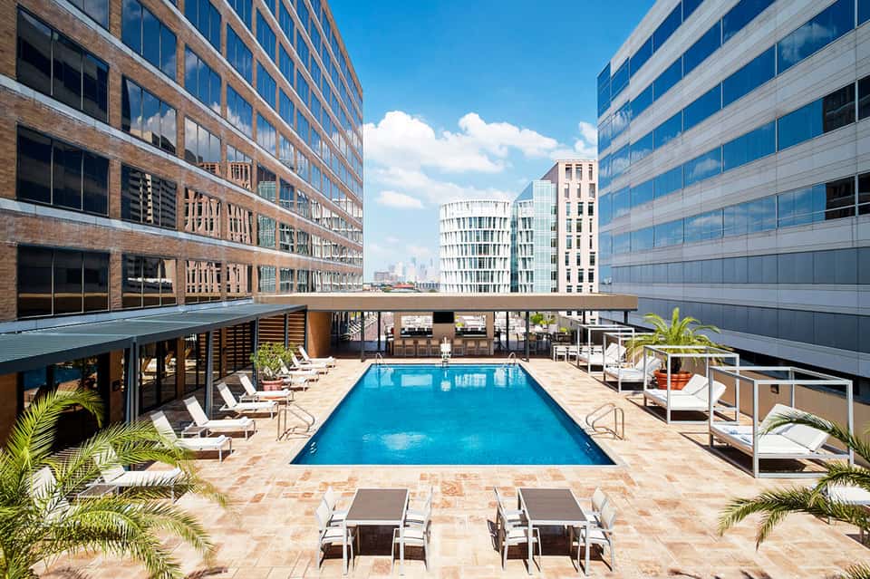 Urban rooftop pool surrounded by high-rise buildings with city skyline views and lounge seating.
