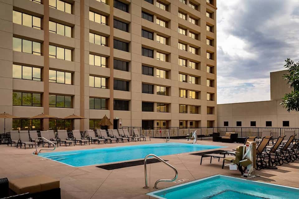 Outdoor pool area with two swimming pools, lounge chairs, and tall tan hotel building backdrop