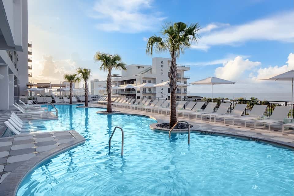 Beachfront hotel pool with palm trees, lounge chairs, and ocean view at sunset