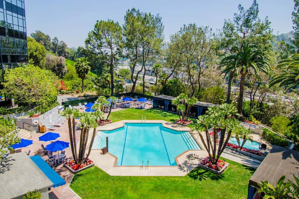 Aerial view of rectangular resort pool surrounded by blue umbrellas and lush landscaping